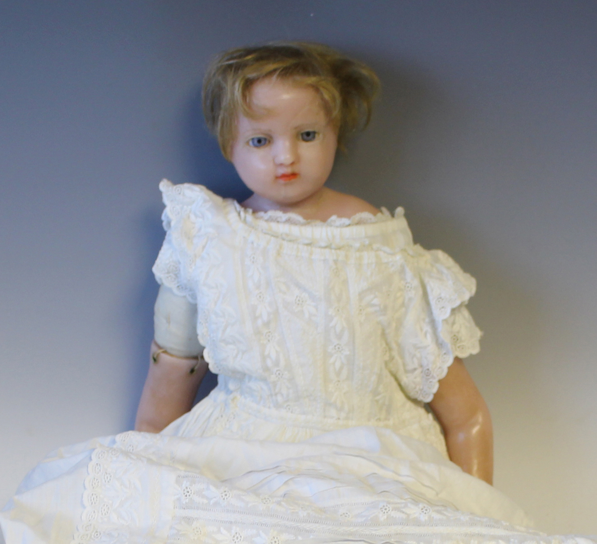 A Pierotti type wax head and shoulders doll with blonde hair, fixed blue eyes, red lips and fabric