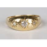 An 18ct gold and diamond three stone ring, star gypsy set with a row of cushion cut diamonds,