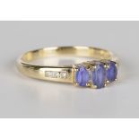 A 9ct gold, tanzanite and diamond ring, claw set with three oval cut tanzanites between diamond