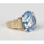A 9ct gold ring, claw set with a circular cut pale blue spinel, the mount with a bark textured