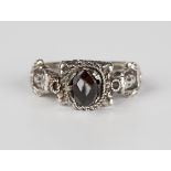 A European silver ring, mounted with a faceted dark garnet, each shoulder decorated with a figure in