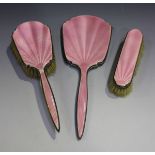 A George V silver and pink enamelled three-piece dressing table set, comprising hand mirror,