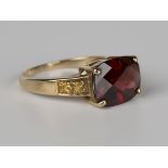 A 9ct gold ring, claw set with a cushion cut garnet between yellow gemstone set two stone shoulders,