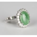 An 18ct white gold, jade and diamond ring, claw set with an oval cabochon jade within a surround