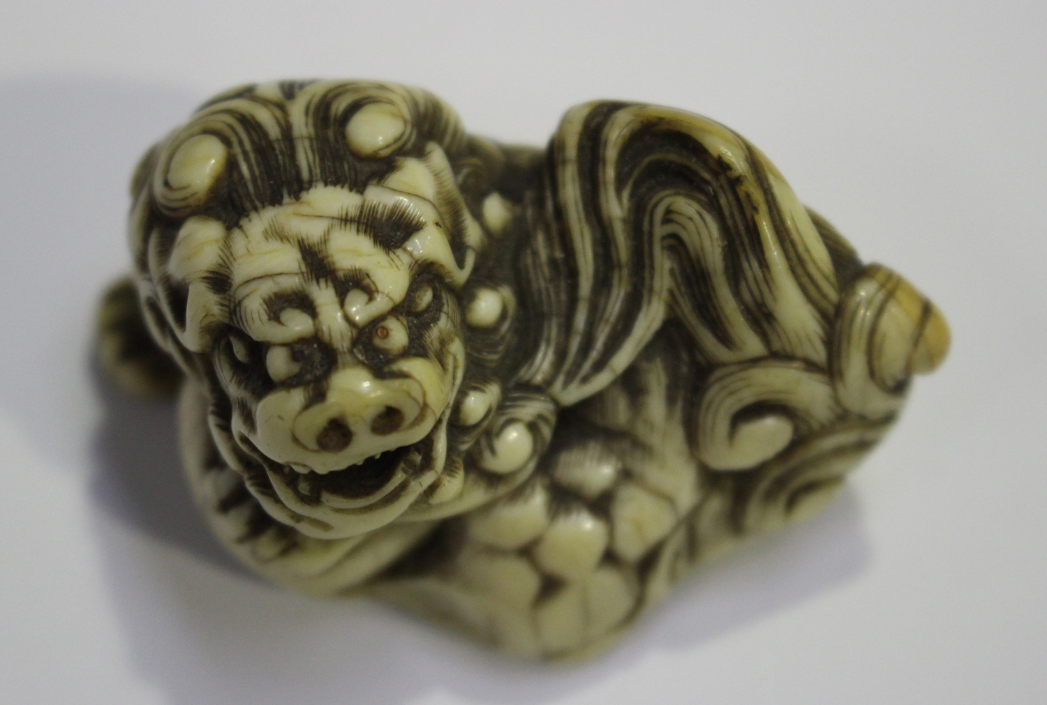 A Japanese carved ivory okimono netsuke, 19th century, modelled as a Buddhistic lion with left paw - Image 2 of 8