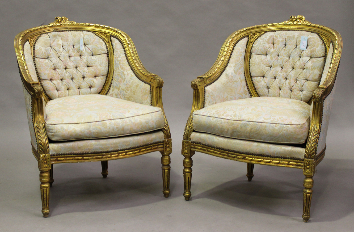 A pair of 20th century Louis XVI style giltwood showframe tub back armchairs, upholstered in foliate