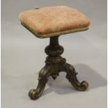 A late Victorian walnut revolving piano stool, the square seat raised on a foliate carved tripod
