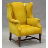 An early 20th century George III style scrolled wing back armchair, upholstered in yellow cord, on