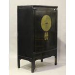 A 20th century Chinese black painted softwood cupboard, the two doors with an applied brass circular