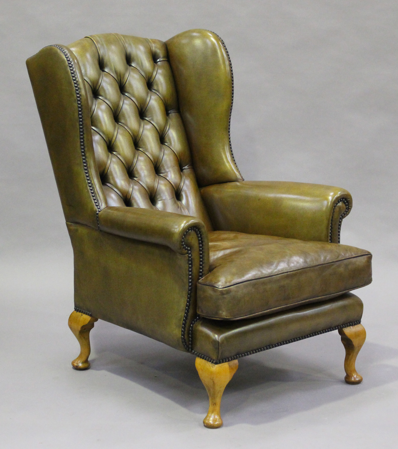 A 20th century George III style wing back armchair, upholstered in buttoned khaki leather, on