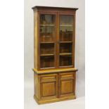 A late Victorian walnut bookcase cabinet, carved with overall bands of flowerheads and stiff leaves,