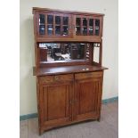 An Arts & Crafts period oak mirrorback side cabinet with upper shelved cupboard enclosed by two