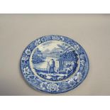 A blue and white plate printed with a man riding a mule beside a river and a group of people on a