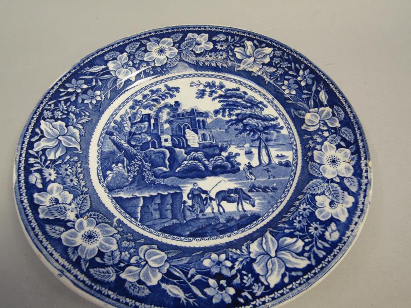 A blue and white plate printed with a scene of travellers and a horse resting bedside a ruined