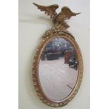 A late 19c gilt wood and stucco wall mirror with eagle mount, the mirror of oval form with a bevel