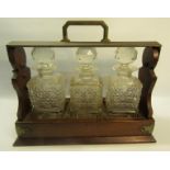 A late Victorian oak three bottle locking tantalus, the clear square bottles half diamond cut,