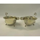A pair of silver sauceboats with shaped top rims and open scrolling handles and on three hoof