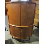 A 1970's teak standing bow front corner cupboard with upper and lower shelves enclosed by hinged
