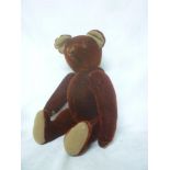 An old burgundy plush covered teddy bear with painted snout, arched back and felt pads,