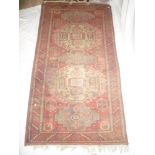 An Eastern hand-knotted wool rug with geometric decoration on red decoration,