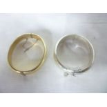 A silver oval bangle with engraved decoration and one other gold plated bangle (2)