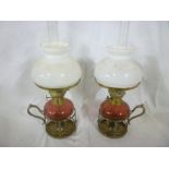 A pair of silver plated chamber candlesticks adapted with brass oil lamps with cranberry tinted