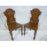 A pair of Victorian carved mahogany hall chairs with scroll backs and polished seats on turned