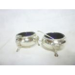 A pair of late Victorian silver circular salts with blue glass liners on hoof feet,