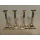 A set of four George V silver Corinthian column candlesticks with fluted stems and square-shaped