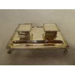 A George V silver rectangular desk stand with twin ink wells enclosed by hinged lids on scroll feet,