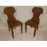 A pair of 19th Century carved mahogany hall chairs with arched backs and polished seats on fluted