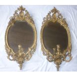 A pair of 19th Century gilt bevelled oval girandole mirrors in ornate gilt relief decorated frames