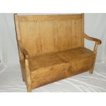 An old polished pine settle with panelled back, box seat with twin hinged lids on block feet,