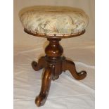 A Victorian walnut revolving piano stool with floral upholstered circular top on tripod base