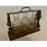 An Edwardian oak three bottle tantalus with electro plated mounts supporting three cut glass