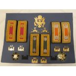 A display of United States Army insignia including brass cap badge, Major Ordnance shoulder boards,