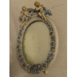 A German porcelain framed oval mirror decorated beneath with flowers below cherub finial,