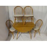 An Ercol light elm circular drop leaf dining table with four light elm spindle back chairs