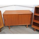 A Danish teak low side cabinet with twin sliding doors, shelved interior, raised on tapering legs,