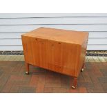 A teak drinks cabinet with lift up twin lids revealing tray interior, single drawer to base,