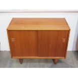A Danish teak small side cabinet with twin sliding doors, raised on tapering legs,