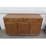 An Ercol side cabinet in light elm and beech, three cupboard doors and twin drawers, on castors.