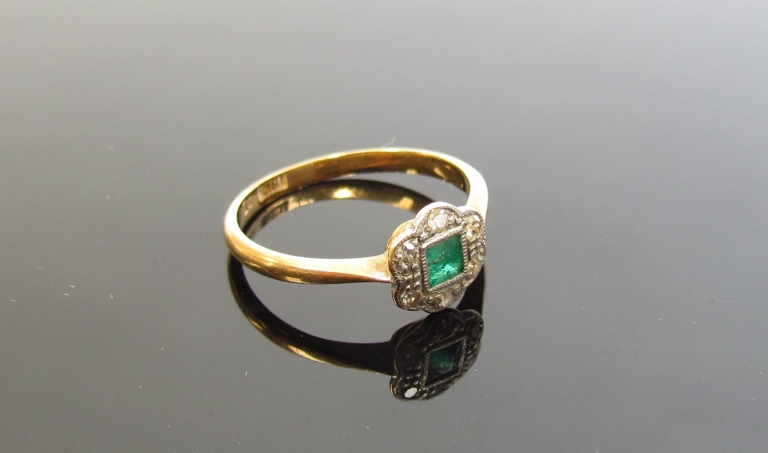 An emerald and diamond set floral ring, the centre square cut emerald framed by small diamonds,