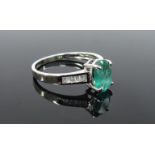 A 9ct white gold ring the oval emerald 7mm x 5mm flanked by a row of baguette cut diamonds in