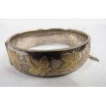 A silver stiff hinge bangle with gold ivy leaf decoration. Birmingham 1963, 18mm wide, 46.