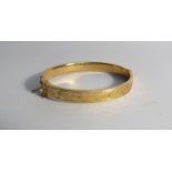 A 9ct gold stiff hinge bangle with foliate engraved detail,