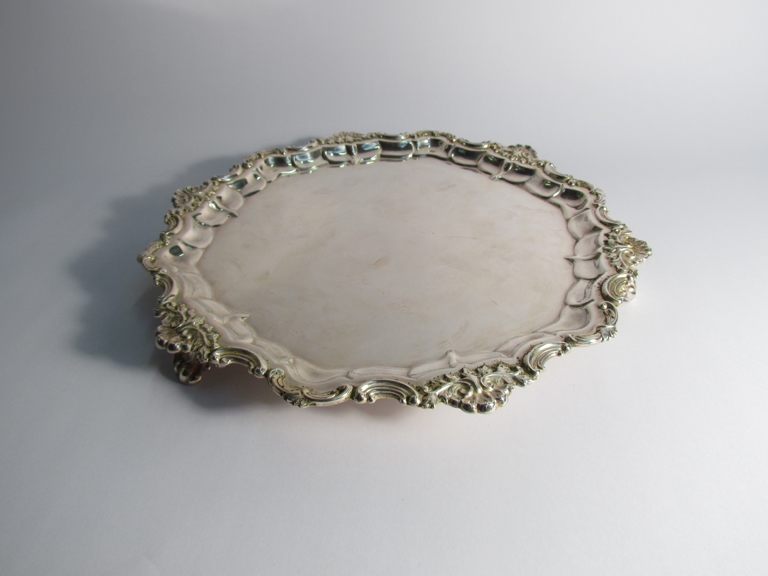 A plated salver with foliate border on scroll feet,