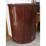 A George III mahogany bow-front wall-hanging corner cupboard with shaped shelves enclosed by a pair