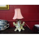 A porcelain figural table lamp depicting maiden and cherubs amongst applied flowers with pink shade