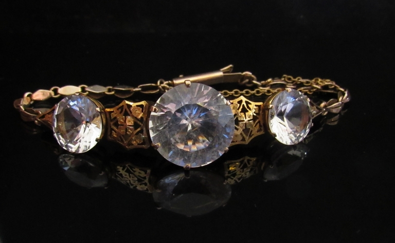 A gold bracelet set with three zircons linked by delicate foliate panels, unmarked, 10.